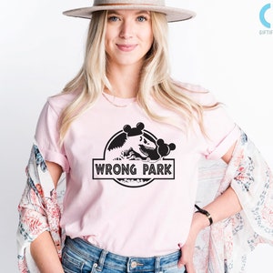 May include: A pink t-shirt with a black graphic of a dinosaur with Mickey Mouse ears and the text "WRONG PARK".