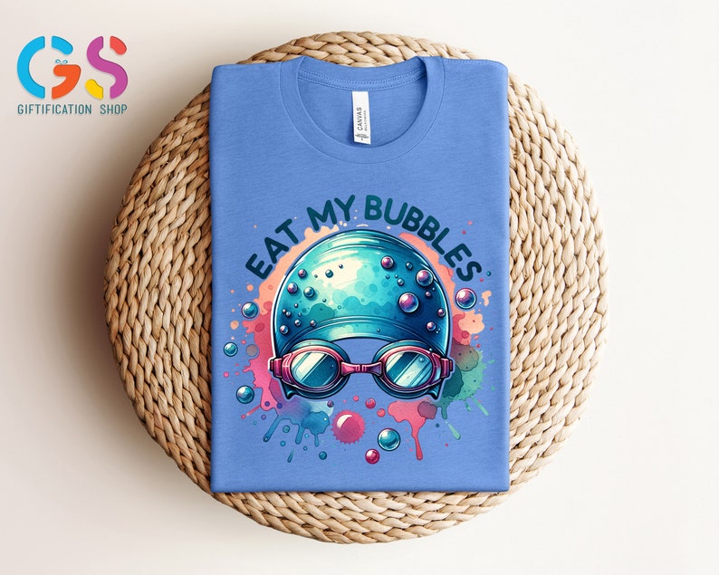 May include: A light blue t-shirt with a colorful graphic of a swimmer's cap and goggles with the text "Eat My Bubbles".