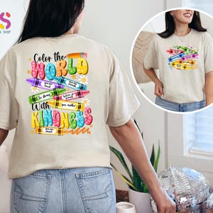 May include: A beige t-shirt with a colorful design on the back. The design features crayons with positive messages, such as "You are loved" and "Believe in yourself." The text "Color the World with Kindness" is also included in the design.
