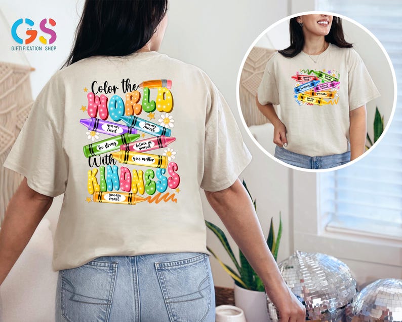 May include: A beige t-shirt with a colorful design on the back. The design features crayons with positive messages, such as "You are loved" and "Believe in yourself." The text "Color the World with Kindness" is also included in the design.