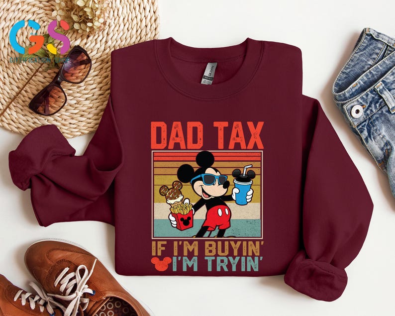 May include: A maroon sweatshirt featuring a graphic of Mickey Mouse wearing sunglasses and holding a drink and fries. The text "DAD TAX" and "IF I'M BUYIN' I'M TRYIN'" are printed above and below the graphic in a vintage style.