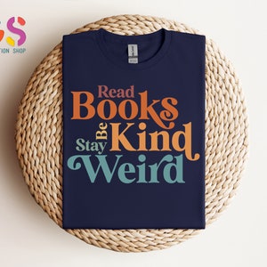 K&ouml;nnte beinhalten: Ein marineblaues T-Shirt mit einer Retro-Grafik, auf der "Read Books Be Kind Stay Weird" steht. Der Text ist in Orange, Gelb und Blau.