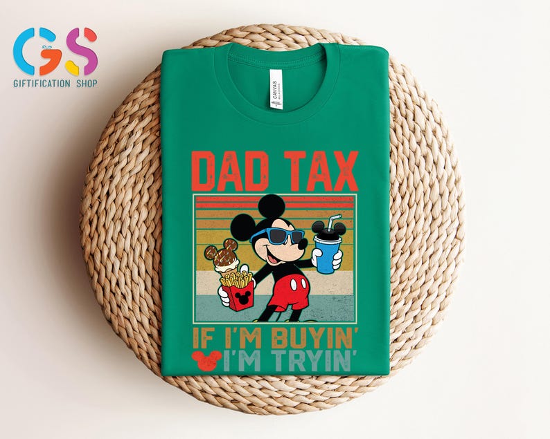 May include: Green t-shirt featuring a graphic of Mickey Mouse wearing sunglasses and holding food and a drink. The text "DAD TAX" is above the graphic, and "IF I'M BUYIN' I'M TRYIN'" is below. The shirt is displayed on a woven surface.