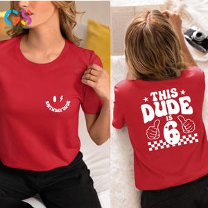May include: Red t-shirt with a white smiley face and the text "Birthday Dude" on the front. The back of the shirt has the text "This Dude is 6" with a thumbs up and a chequered pattern.