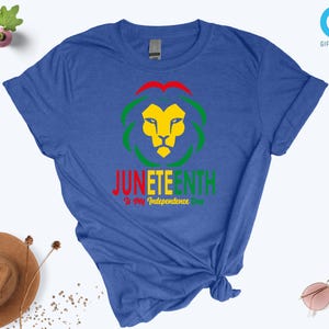 Pode incluir: Camiseta azul com um desenho de le&atilde;o em amarelo, verde e vermelho, e o texto "Juneteenth: Is My Independence Day". Uma pe&ccedil;a de roupa casual.