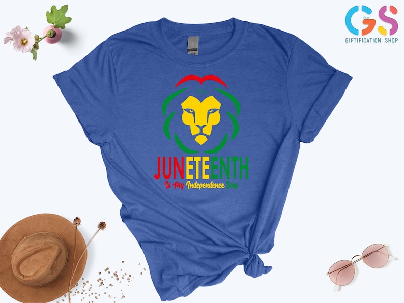 Pode incluir: Camiseta azul com um desenho de le&atilde;o em amarelo, verde e vermelho, e o texto "Juneteenth: Is My Independence Day". Uma pe&ccedil;a de roupa casual.