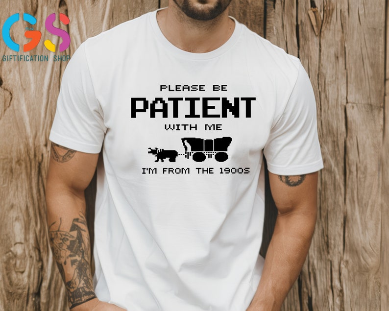 Puede incluir: Camiseta blanca con texto negro que dice "Por favor, ten paciencia conmigo, soy de los a&ntilde;os 1900". El texto est&aacute; en una fuente pixelada. Debajo del texto hay una ilustraci&oacute;n en blanco y negro de un carro tirado por un toro.
