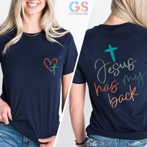 May include: Navy blue t-shirt with a heart and cross on the front and the text "Jesus has my back" on the back. The text is in a colorful script font.