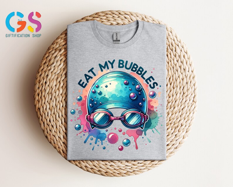 May include: A gray t-shirt with a blue and white swimming cap and goggles with the text "Eat My Bubbles" in a colorful watercolor design.