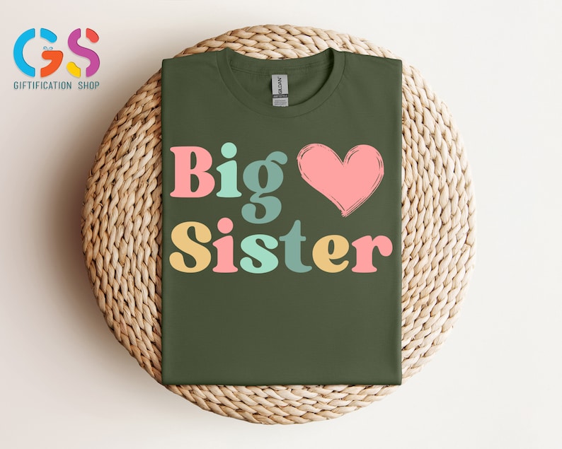 May include: A green t-shirt with the text "Big Sister" in colorful letters and a pink heart.