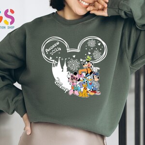 Pode incluir: Camisola verde com um design branco da cabe&ccedil;a do Mickey Mouse, o texto "Andrew 2026" e personagens da Disney. O design inclui fogos de artif&iacute;cio e uma silhueta de castelo. A camisola &eacute; de cor verde lisa.