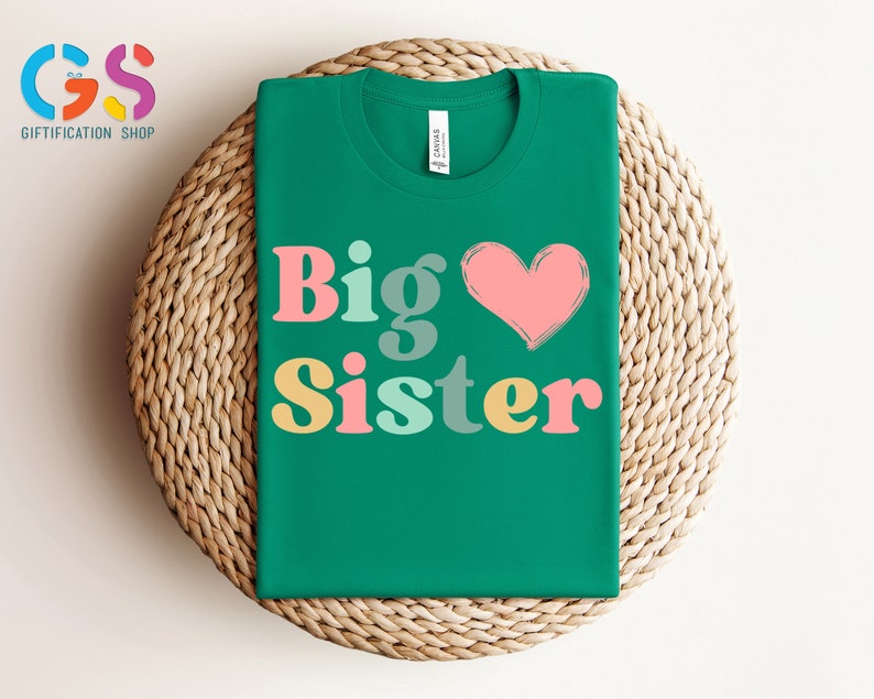 May include: A green t-shirt with the text "Big Sister" in colorful letters and a pink heart.