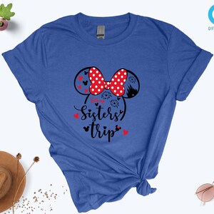 Puede incluir: Una camiseta azul real con un gr&aacute;fico en blanco y negro de orejas de Mickey Mouse con un lazo rojo y el texto "Sisters' Trip".