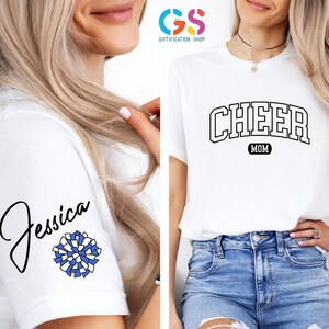 May include: White t-shirt with the text "CHEER MOM" in a black varsity-style font. The shirt also has a blue and white pom-pom and the name "Jessica" written in black cursive on the sleeve.