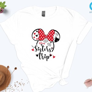 Puede incluir: Camiseta blanca con un gr&aacute;fico de cabeza de Minnie Mouse rojo y negro y el texto "Disney Sisters' Trip".