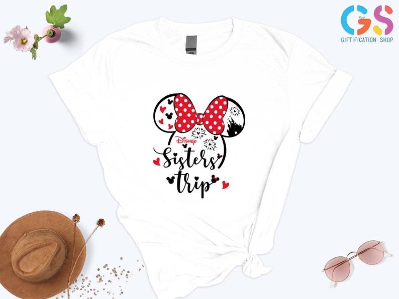 Puede incluir: Camiseta blanca con un gr&aacute;fico de cabeza de Minnie Mouse rojo y negro y el texto "Disney Sisters' Trip".