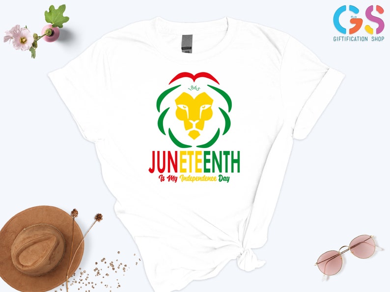 Pode incluir: Camiseta branca com um design colorido para o Juneteenth. O design inclui uma cabe&ccedil;a de le&atilde;o amarela, detalhes verdes e vermelhos e o texto "Juneteenth Is My Independence Day."