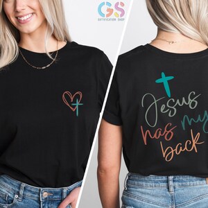 May include: Black t-shirt with a heart and cross on the front and the text "Jesus has my back" on the back. The text is in a colorful, handwritten style.