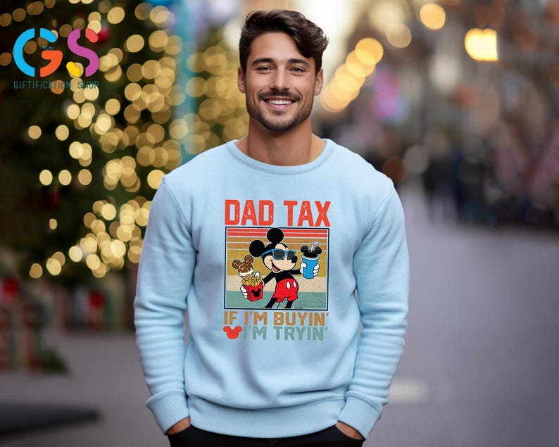 May include: Light blue sweatshirt featuring a graphic of Mickey Mouse wearing sunglasses, holding a drink and fries, with the text "DAD TAX" and "IF I'M BUYIN' I'M TRYIN'". The sweatshirt is a crew neck style.