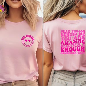 May include: Pink t-shirt with a pink smiley face with hearts for eyes and the text "You Matter" on the front. The back of the shirt has the text "Dear person behind me you are amazing beautiful enough remember that" in pink.
