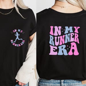 May include: Black t-shirt with the text "In My Runner Era" in pink and blue letters with a running figure in the center. The text is in a retro font style.