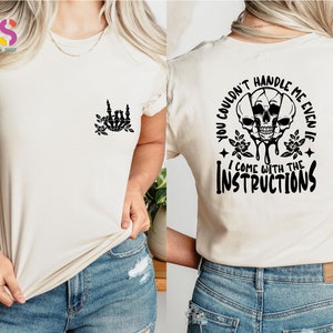 Op de afbeelding: Een wit T-shirt met een zwarte schedelprint en de tekst "You couldn't handle me even if I come with the instructions".