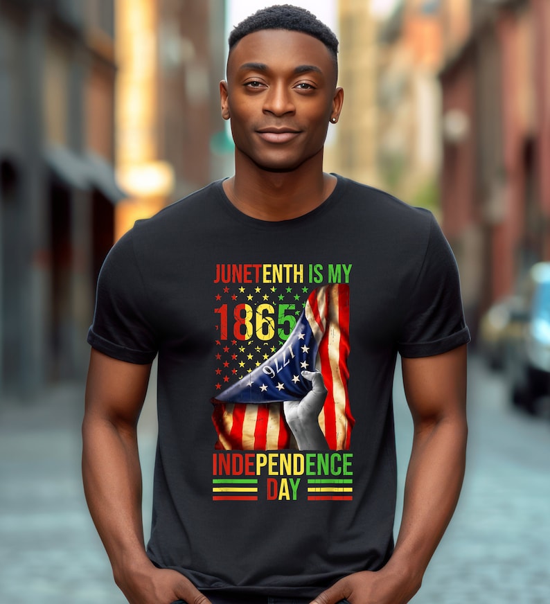 Puede incluir: Camiseta negra con el texto "Juneteenth is my 1865 Independence Day" en rojo, amarillo, verde y negro. El dise&ntilde;o incluye una mano sosteniendo una bandera estadounidense ondeando.