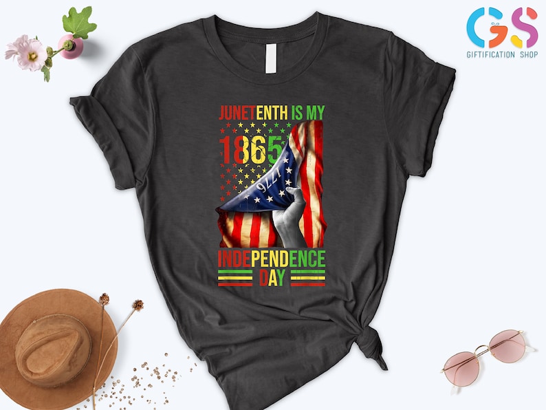 Puede incluir: Camiseta gris oscuro con un dise&ntilde;o gr&aacute;fico que celebra el Juneteenth. El dise&ntilde;o incluye el texto "Juneteenth is my 1865 Independence Day" con una bandera estadounidense y estrellas.