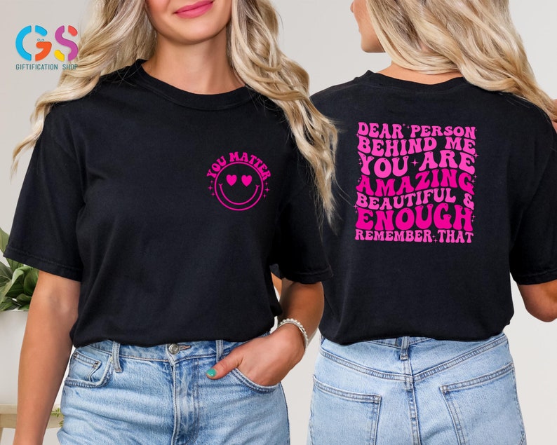 May include: Two black t-shirts with pink text. The front shirt says "You Matter" with a smiley face and hearts for eyes. The back shirt says "Dear Person Behind Me You Are Amazing Beautiful & Enough Remember That".