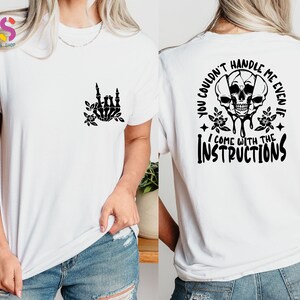 Op de afbeelding: Wit T-shirt met een zwart skelet handontwerp aan de voorkant en een schedelgrafiek met de tekst "You couldn't handle me even if I come with the instructions" aan de achterkant.