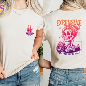 May include: White t-shirt with a pink and purple skeleton graphic holding a drink and the text "Expensive and Talks Back".