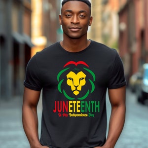 Pode incluir: Camiseta preta com um desenho de cabe&ccedil;a de le&atilde;o em amarelo, verde e vermelho, com o texto "Juneteenth Is My Independence Day". O design inclui o ano de 1865. A camiseta &eacute; de gola redonda.