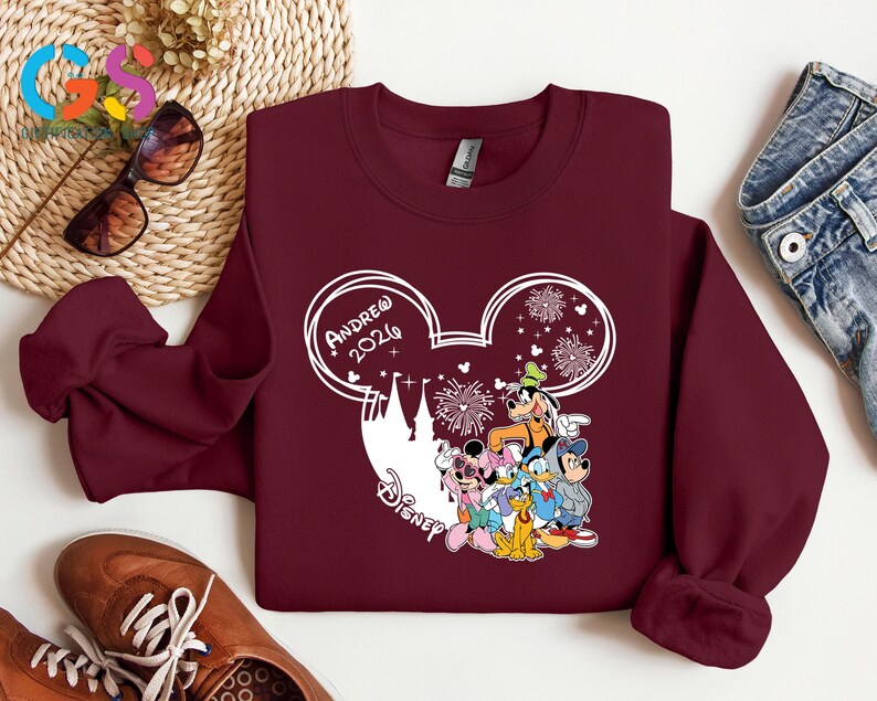 Pode incluir: Um moletom bord&ocirc; com um design branco da cabe&ccedil;a do Mickey Mouse, o texto "Andrew 2026" e uma silhueta do castelo da Disney. O design inclui personagens da Disney e fogos de artif&iacute;cio.