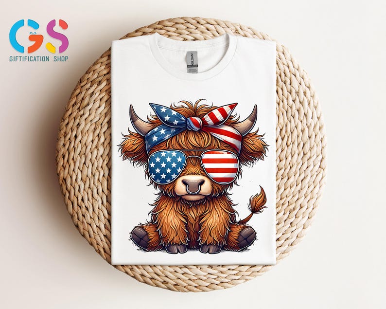 Puede incluir: Camiseta blanca con un dibujo de una vaca de las Tierras Altas con gafas de sol y una diadema con un dise&ntilde;o de la bandera estadounidense. La vaca tiene pelaje marr&oacute;n y est&aacute; sentada. La camiseta est&aacute; doblada sobre una superficie tejida.