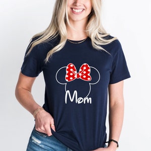 May include: A navy blue t-shirt with a white outline of Mickey Mouse ears and a red bow with white polka dots. The text "Mom" is printed in white below the ears.