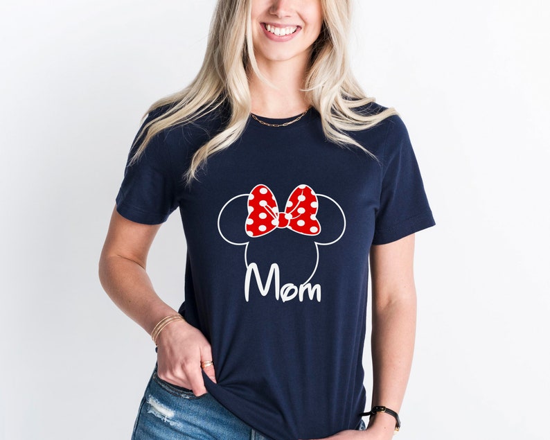 May include: A navy blue t-shirt with a white outline of Mickey Mouse ears and a red bow with white polka dots. The text "Mom" is printed in white below the ears.