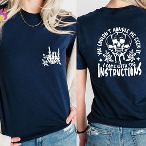 Op de afbeelding: Een marineblauw t-shirt met een witte schedel en een bloemenontwerp op de achterkant. De tekst op de achterkant luidt "You couldn't handle me even if I come with the instructions". De voorkant van het shirt heeft een witte skelethand met bloemen.