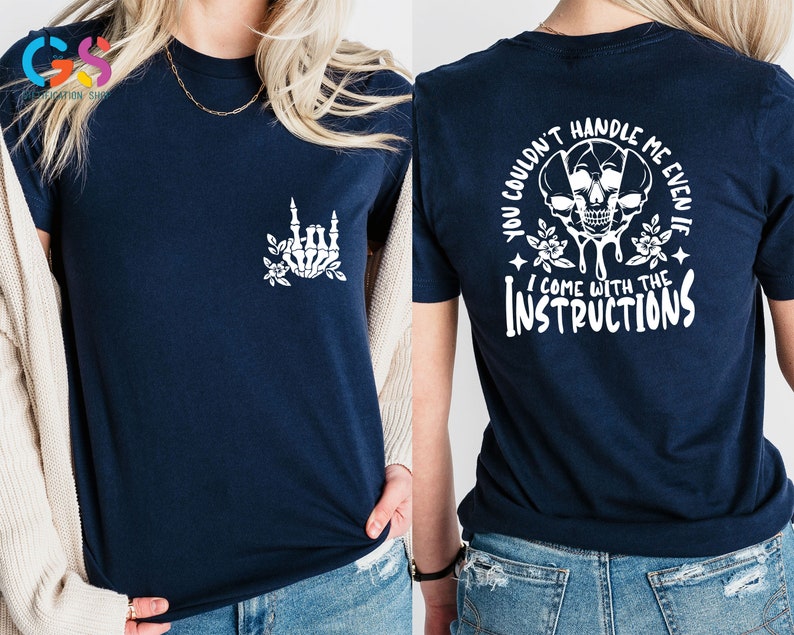 Op de afbeelding: Een marineblauw t-shirt met een witte schedel en een bloemenontwerp op de achterkant. De tekst op de achterkant luidt "You couldn't handle me even if I come with the instructions". De voorkant van het shirt heeft een witte skelethand met bloemen.