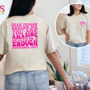 May include: Two beige t-shirts with pink text. The front shirt says "You Matter" with a pink smiley face. The back shirt says "Dear person behind me you are amazing beautiful & enough remember that".
