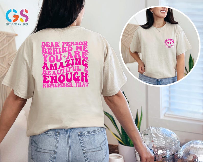 May include: Two beige t-shirts with pink text. The front shirt says "You Matter" with a pink smiley face. The back shirt says "Dear person behind me you are amazing beautiful & enough remember that".