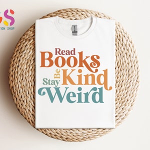K&ouml;nnte beinhalten: Wei&szlig;es T-Shirt mit dem Text "Read Books Be Kind Stay Weird" in bunter Retro-Schrift.