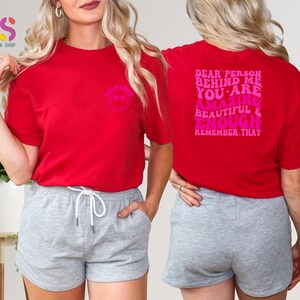 May include: Red t-shirt with a pink smiley face on the front and the text "Dear person behind me you are amazing beautiful & enough remember that" on the back.
