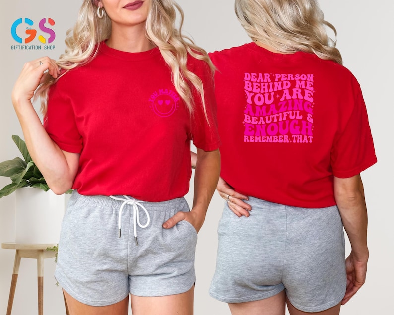 May include: Red t-shirt with a pink smiley face on the front and the text "Dear person behind me you are amazing beautiful & enough remember that" on the back.