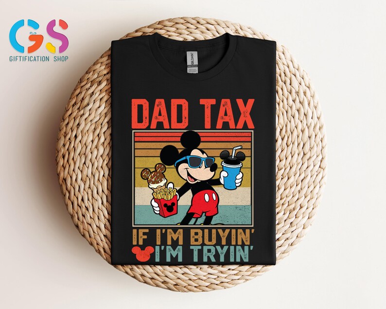 May include: Black t-shirt featuring Mickey Mouse wearing sunglasses and holding a drink and fries. The text "DAD TAX" is above the image, with "IF I'M BUYIN' I'M TRYIN'" below. The design has a retro, vintage style.
