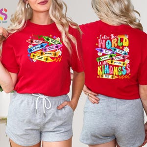 May include: Red t-shirt with a design of colorful crayons with the text "Color the World with Kindness" on the front. The back of the shirt has a design of crayons with positive messages.