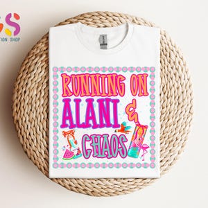 Puede incluir: Camiseta blanca con el texto "RUNNING ON ALANI & CHAOS" en rosa y naranja, con gr&aacute;ficos coloridos de un zapato, un p&aacute;jaro y una bebida. La camiseta se muestra sobre una superficie circular tejida.