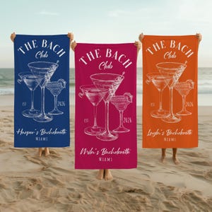 May include: Three beach towels in blue, fuchsia, and orange, each with a white illustration of martini glasses. The text "THE BACH Club" and "2026" are visible. The blue towel says "Harper's Bachelorette Miami".