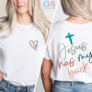 May include: White t-shirt with a red heart and a teal cross on the front and the text "Jesus has my back" in teal, green, and orange on the back.