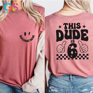 May include: Pink t-shirt with a black smiley face and the text "Birthday Dude" on the front and the text "This Dude is 6" with a black number 6 and two thumbs up on the back.