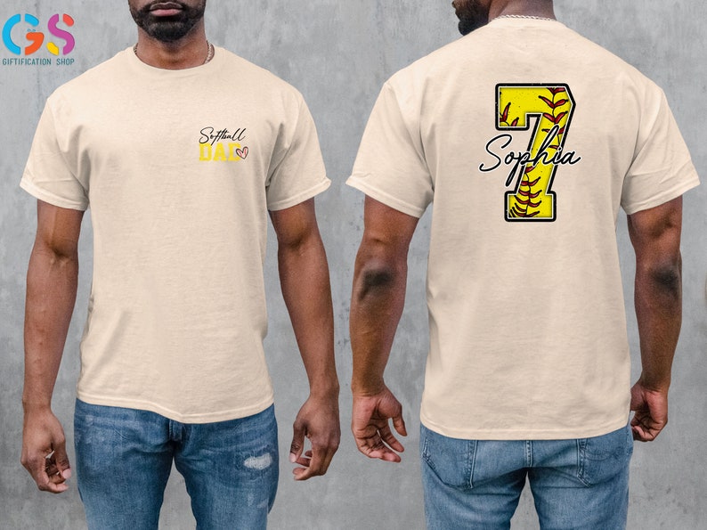 May include: A beige t-shirt with the text "Softball Dad" and a small heart on the front. The back of the shirt has a yellow softball with the number 7 and the name "Sophia" written in cursive.